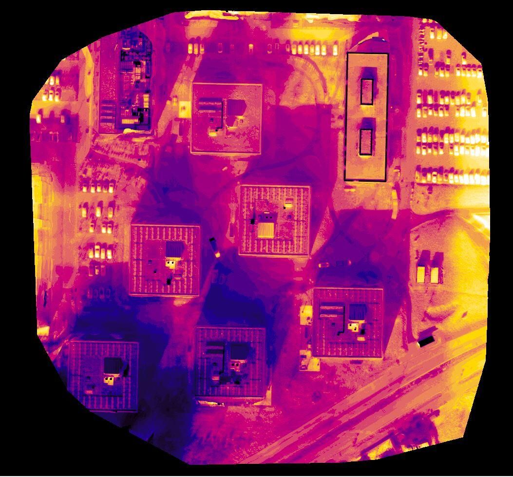 Thermal map of several building rooftops and a parking area seen from above.